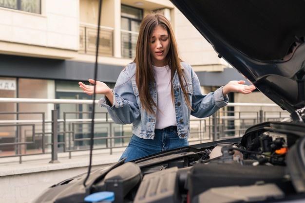 Young worried girl is using a phone to explain the mechanic the problem with a car that she has. Free Photo